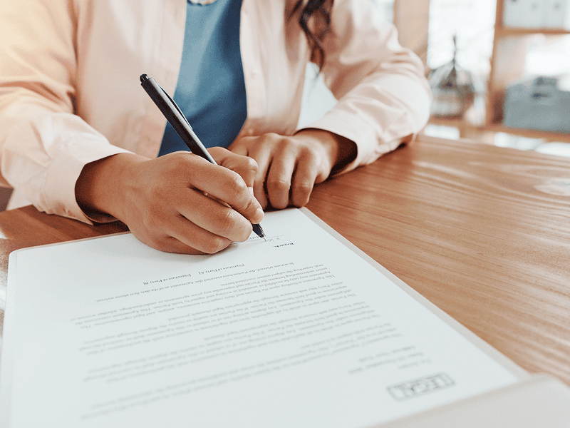Person signing a document at desk.