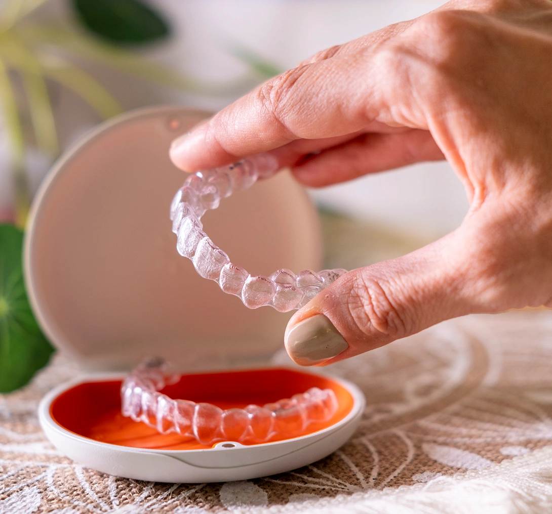 Hand holding clear dental aligner above case.