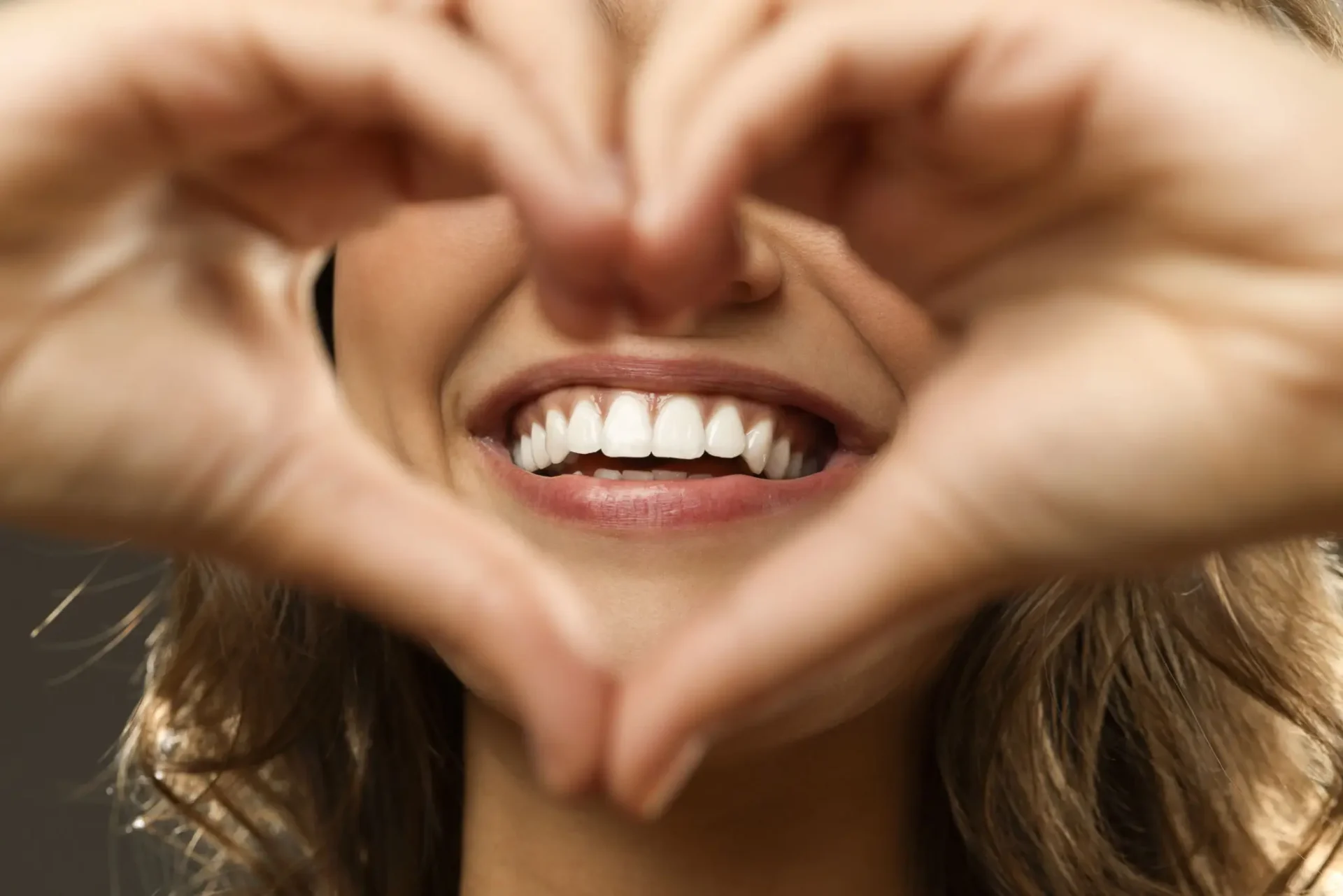 Smiling face framed by heart-shaped hands.